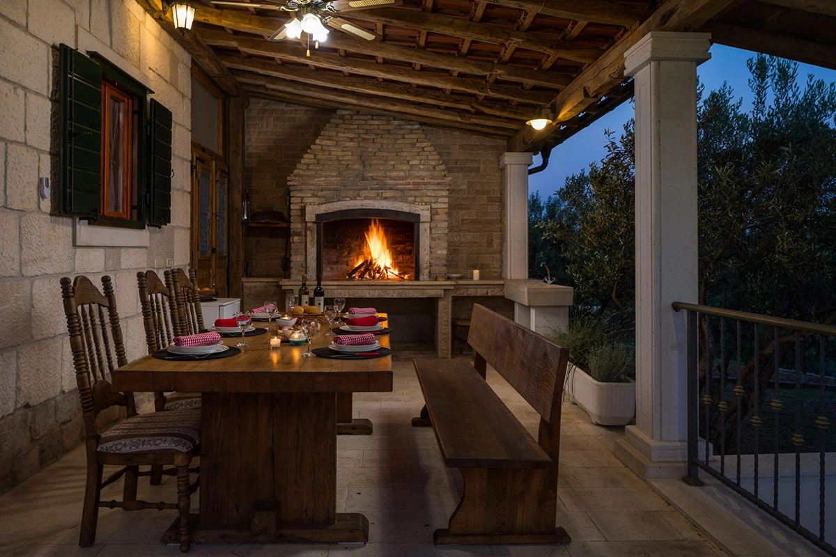 Outdoor dining table in front of the villa with a traditional Croatian barbecue and a lit fire.